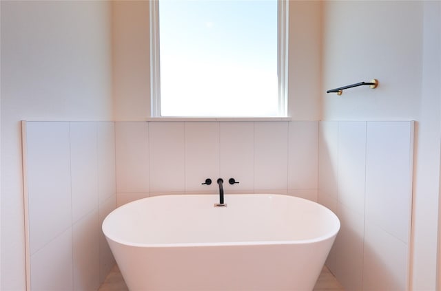 bathroom with tile walls, a soaking tub, and wainscoting