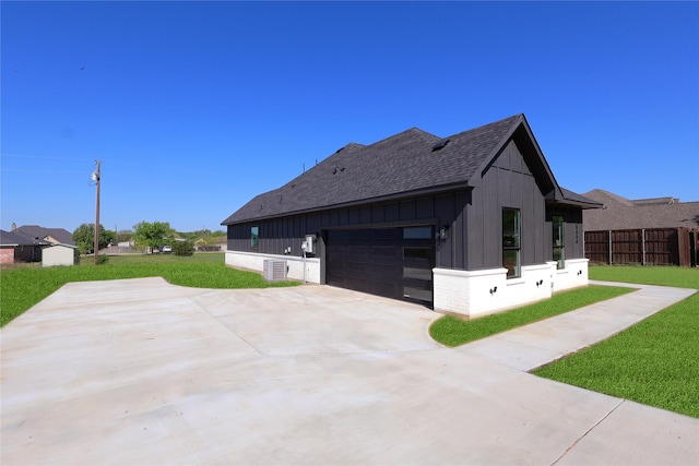 view of side of home with board and batten siding, a lawn, fence, an attached garage, and driveway