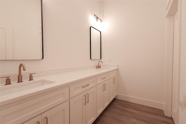 full bath featuring a sink, baseboards, double vanity, and wood finished floors