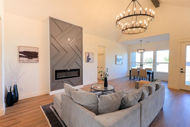 living room with a large fireplace, vaulted ceiling, a chandelier, wood finished floors, and baseboards