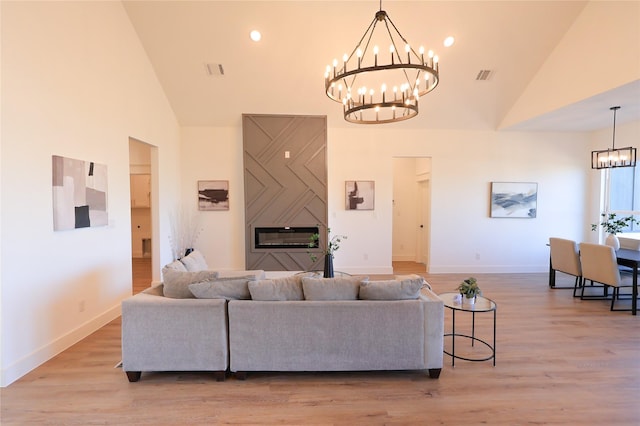 living room with high vaulted ceiling, light wood finished floors, a notable chandelier, and visible vents