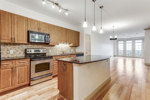 3818 Holland Ave Unit 305, Dallas, TX 75219 - kitchen featuring a notable chandelier, light wood-style floors, dark stone counters, decorative backsplash, and appliances with stainless steel finishes