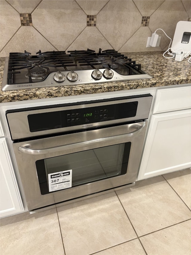 kitchen view of appliances with stainless steel finishes, white cabinets, tasteful backsplash, and dark stone countertops