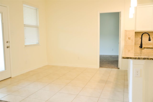 unfurnished room featuring a sink, light tile patterned flooring, and baseboards