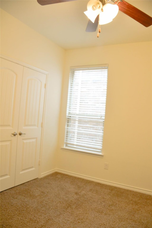 carpeted empty room with ceiling fan and baseboards