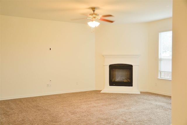 unfurnished living room with carpet floors, a glass covered fireplace, a ceiling fan, and baseboards