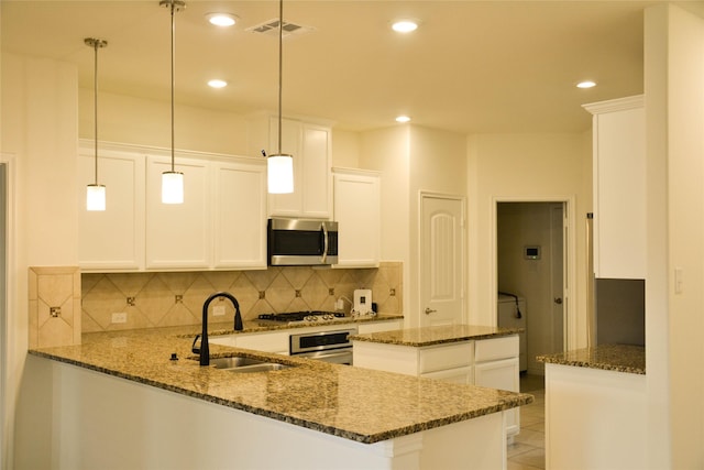 kitchen with appliances with stainless steel finishes, a sink, decorative backsplash, dark stone countertops, and a peninsula