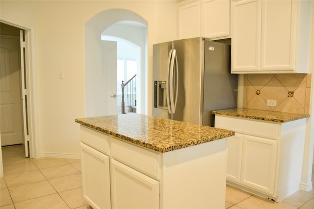 kitchen featuring stainless steel fridge with ice dispenser, arched walkways, stone counters, and light tile patterned flooring