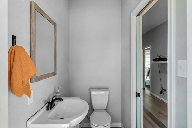 half bath featuring a sink, baseboards, toilet, and wood finished floors