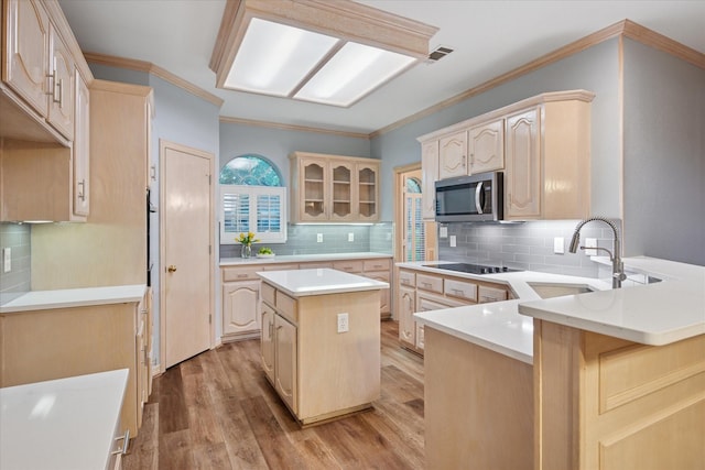kitchen with a sink, stainless steel microwave, black electric cooktop, a peninsula, and light brown cabinets