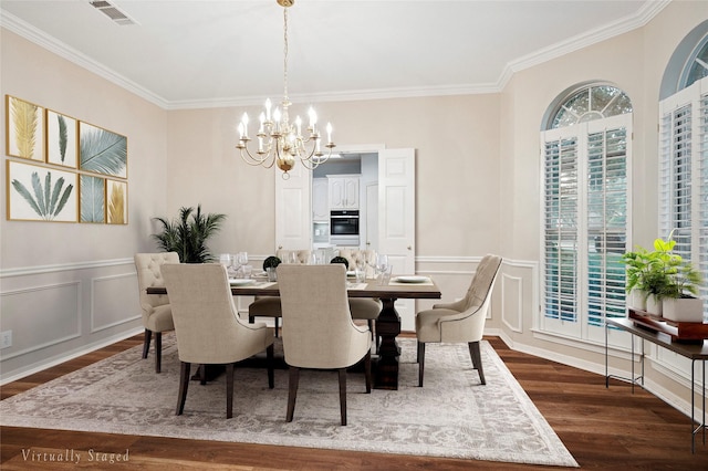 dining room with a chandelier, ornamental molding, dark wood-style flooring, a decorative wall, and wainscoting