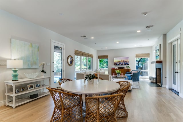dining space with visible vents, a fireplace with flush hearth, light wood finished floors, and a wealth of natural light