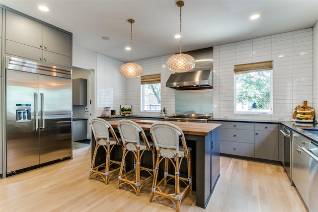 kitchen with built in refrigerator, butcher block counters, gray cabinets, and light wood-style flooring