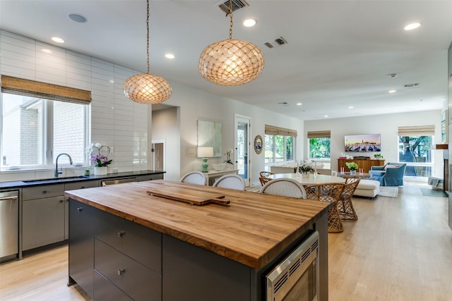 kitchen with stainless steel microwave, butcher block countertops, a sink, and visible vents