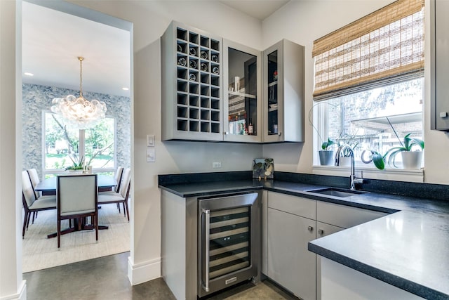 bar with beverage cooler, a notable chandelier, plenty of natural light, and a sink