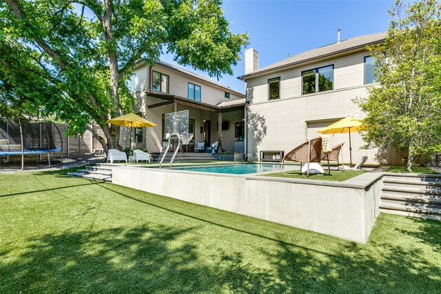 back of property featuring a trampoline, brick siding, an outdoor pool, a chimney, and a yard