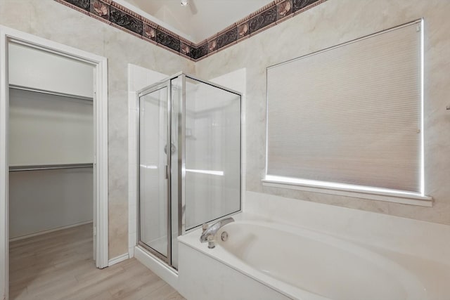 full bathroom featuring a stall shower, a walk in closet, wood finished floors, and a bath