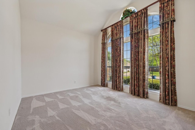carpeted spare room featuring baseboards and high vaulted ceiling