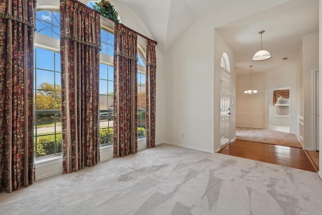 carpeted empty room with healthy amount of natural light, high vaulted ceiling, a chandelier, a decorative wall, and a wainscoted wall