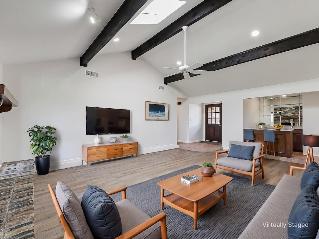 living room featuring baseboards, vaulted ceiling with beams, visible vents, and light wood-style flooring