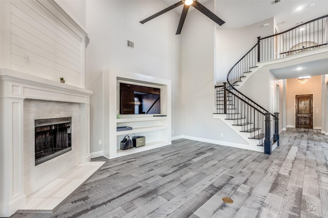 8321 Burnley, The Colony, TX 75056 - unfurnished living room with stairs, wood finished floors, a towering ceiling, ceiling fan, and a fireplace with flush hearth