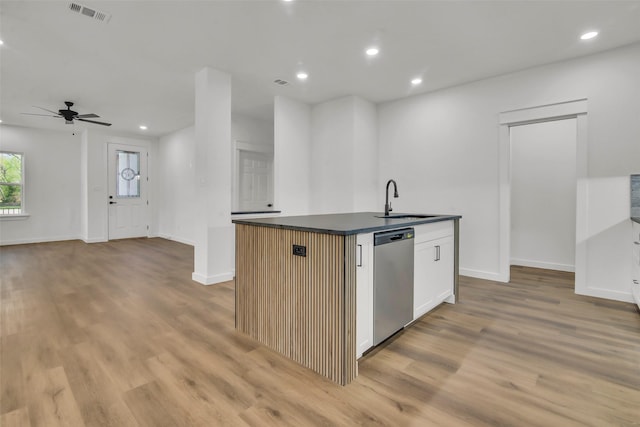 kitchen featuring light wood-style flooring, dark countertops, a kitchen island with sink, visible vents, and stainless steel dishwasher
