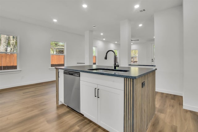 kitchen with dark countertops, a kitchen island with sink, a healthy amount of sunlight, dishwasher, and a sink