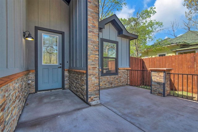 doorway to property featuring board and batten siding, fence, and a patio