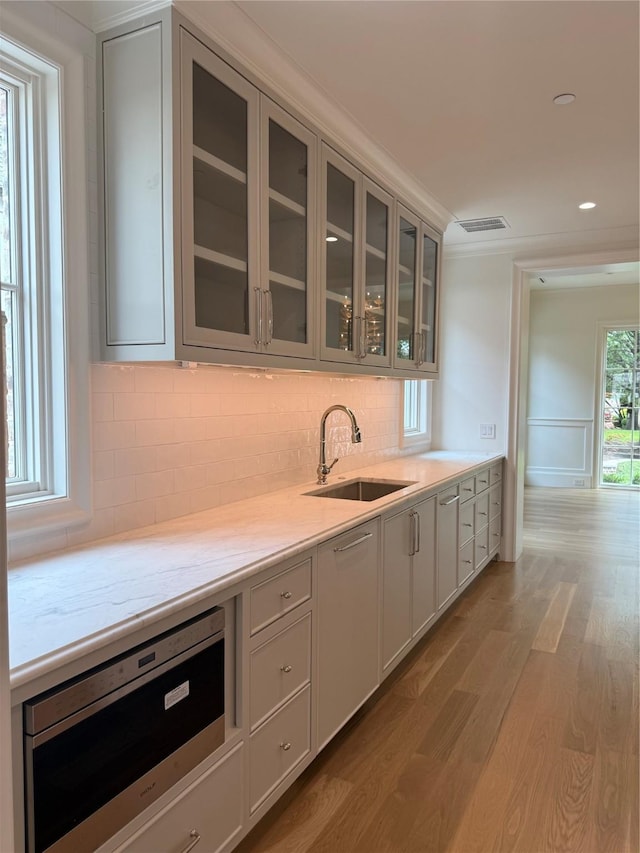 kitchen featuring a sink, wood finished floors, tasteful backsplash, glass insert cabinets, and recessed lighting