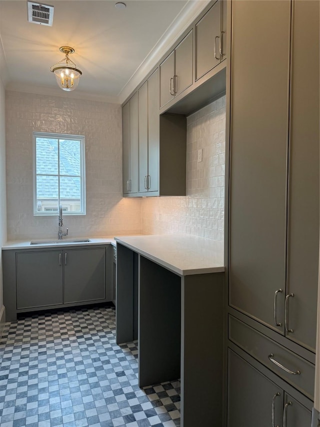 kitchen with gray cabinetry, light flooring, light countertops, a sink, and crown molding