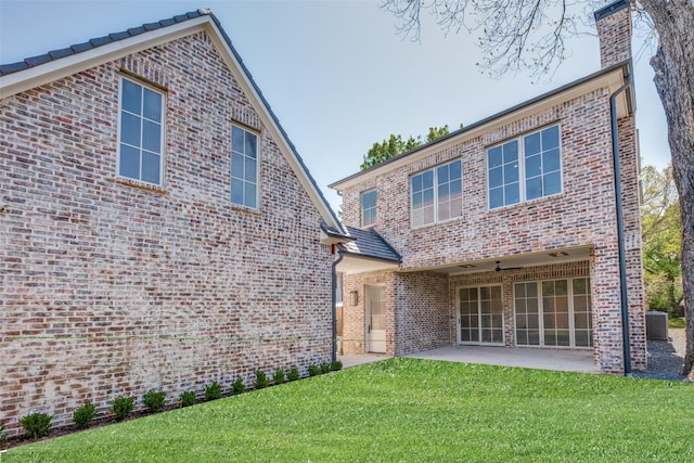 rear view of property featuring a patio area, brick siding, a lawn, a chimney, and central AC unit