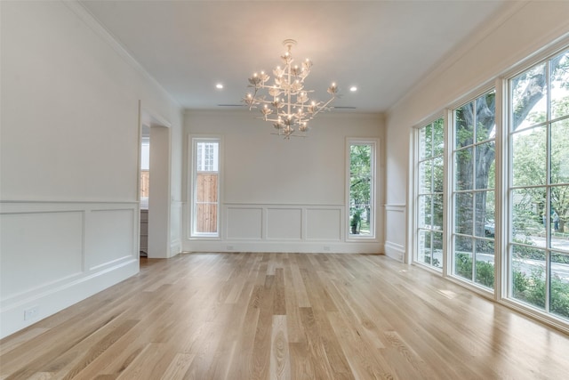 unfurnished dining area featuring a chandelier, ornamental molding, healthy amount of natural light, a decorative wall, and light wood finished floors