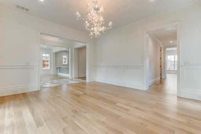 unfurnished dining area featuring ornamental molding, a decorative wall, healthy amount of natural light, a chandelier, and light wood-style flooring