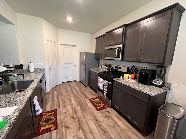 kitchen featuring a sink, appliances with stainless steel finishes, light wood-style floors, dark brown cabinets, and light stone countertops