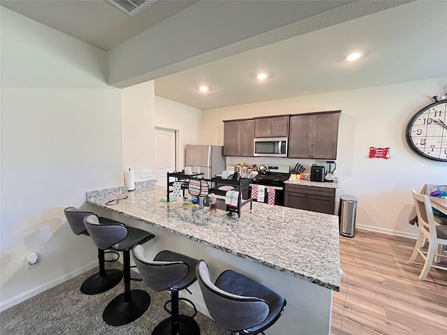 kitchen featuring baseboards, a kitchen breakfast bar, dark brown cabinetry, a peninsula, and stainless steel appliances