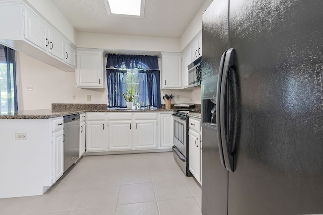 kitchen with white cabinetry, appliances with stainless steel finishes, plenty of natural light, and dark stone counters