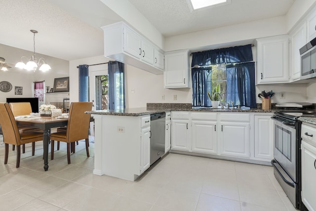 kitchen with dark stone countertops, an inviting chandelier, appliances with stainless steel finishes, a peninsula, and white cabinetry