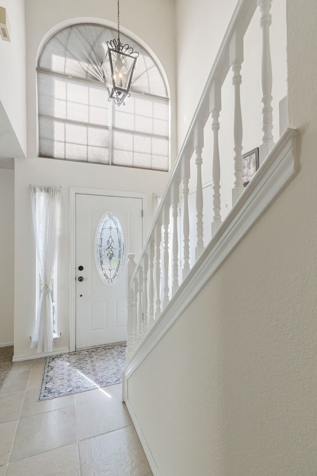 tiled foyer entrance featuring stairs, baseboards, a towering ceiling, and a notable chandelier