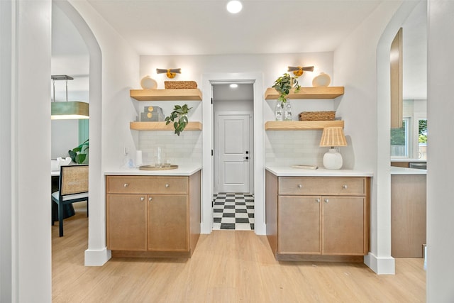 bar with arched walkways, tasteful backsplash, and light wood-style floors