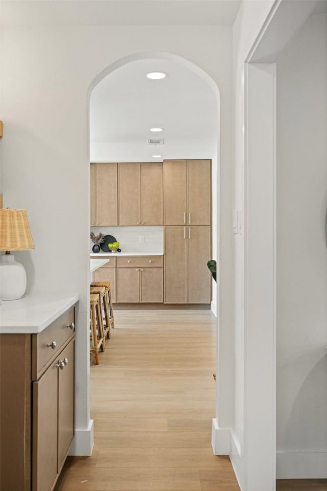 hall featuring baseboards, light wood finished floors, and arched walkways
