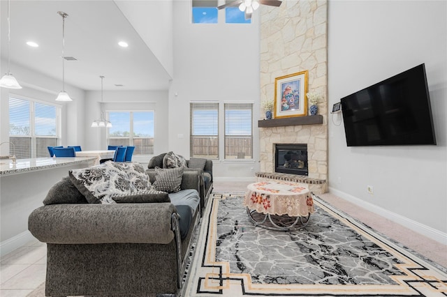 living room with a towering ceiling, a ceiling fan, visible vents, a stone fireplace, and baseboards