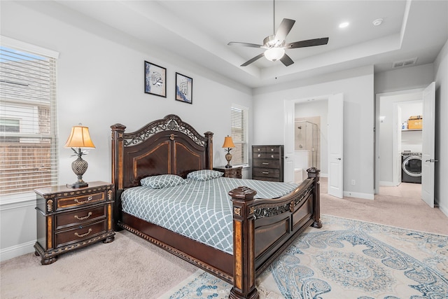 bedroom with washer / clothes dryer, multiple windows, light colored carpet, and a raised ceiling