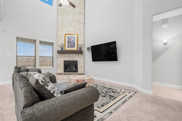 carpeted living room with a fireplace, a high ceiling, baseboards, and ceiling fan