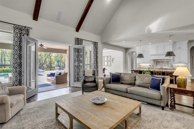 living room featuring beamed ceiling, light wood finished floors, arched walkways, and a ceiling fan