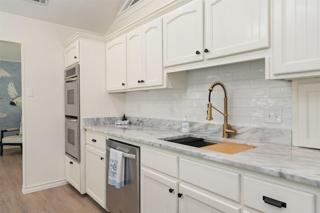 kitchen featuring light stone countertops, light wood-type flooring, a sink, stainless steel appliances, and decorative backsplash