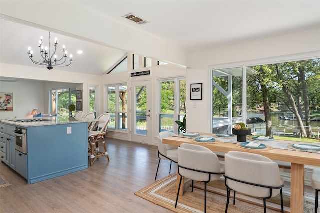 dining space with an inviting chandelier, light wood-type flooring, vaulted ceiling, visible vents, and a water view