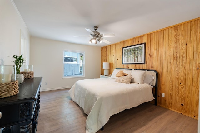 bedroom featuring wooden walls, baseboards, a ceiling fan, and wood finished floors