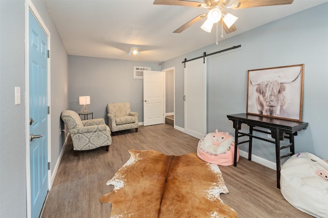 sitting room with wood finished floors, ceiling fan, baseboards, and a barn door