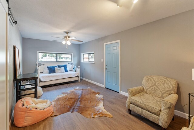 bedroom with a barn door, baseboards, a ceiling fan, and wood finished floors
