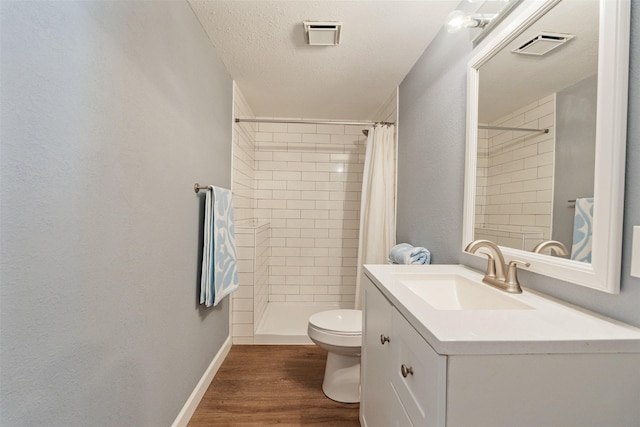 full bath with vanity, toilet, tiled shower, visible vents, and wood finished floors